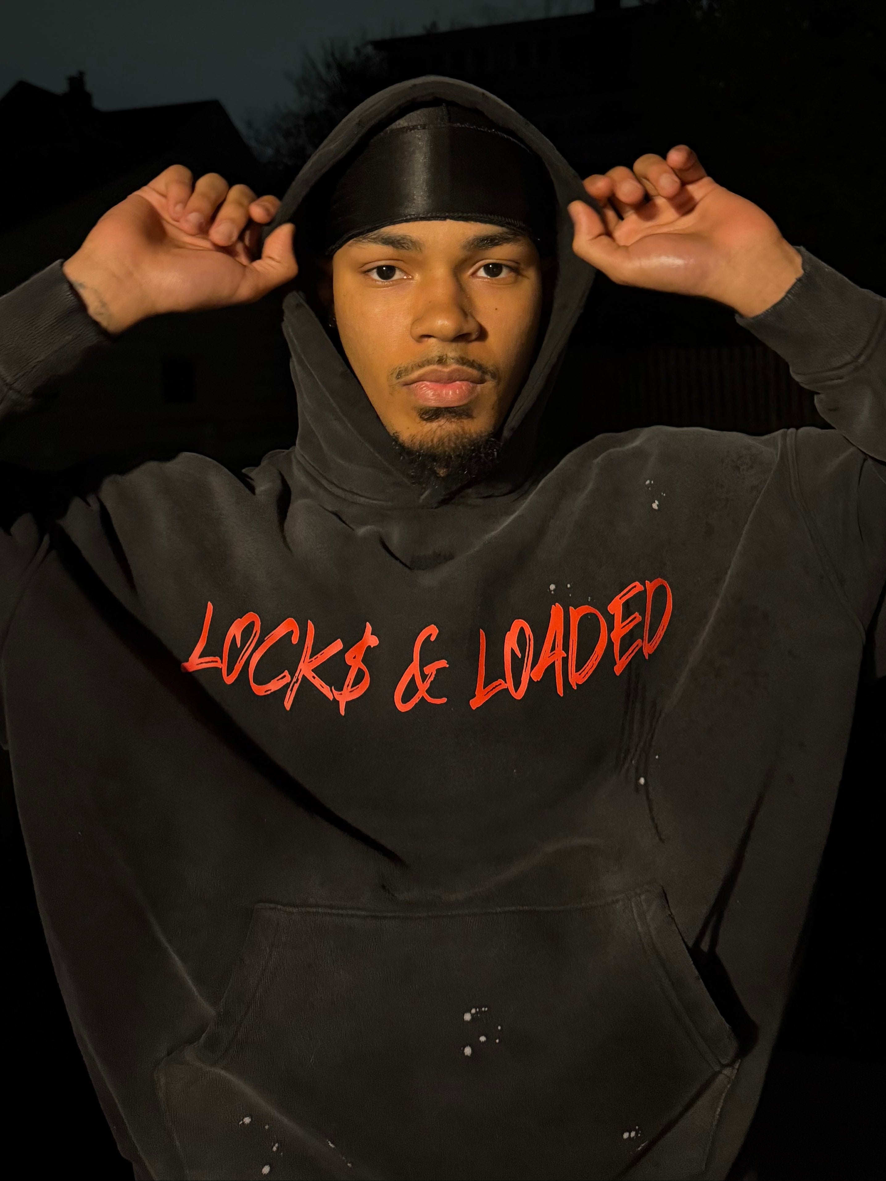 Person wearing a black hoodie with 'LOCKED & LOADED' text in red, standing against a dark background